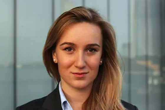 Maria Zhivitskaya stands in front of large glass windows wearing a suit