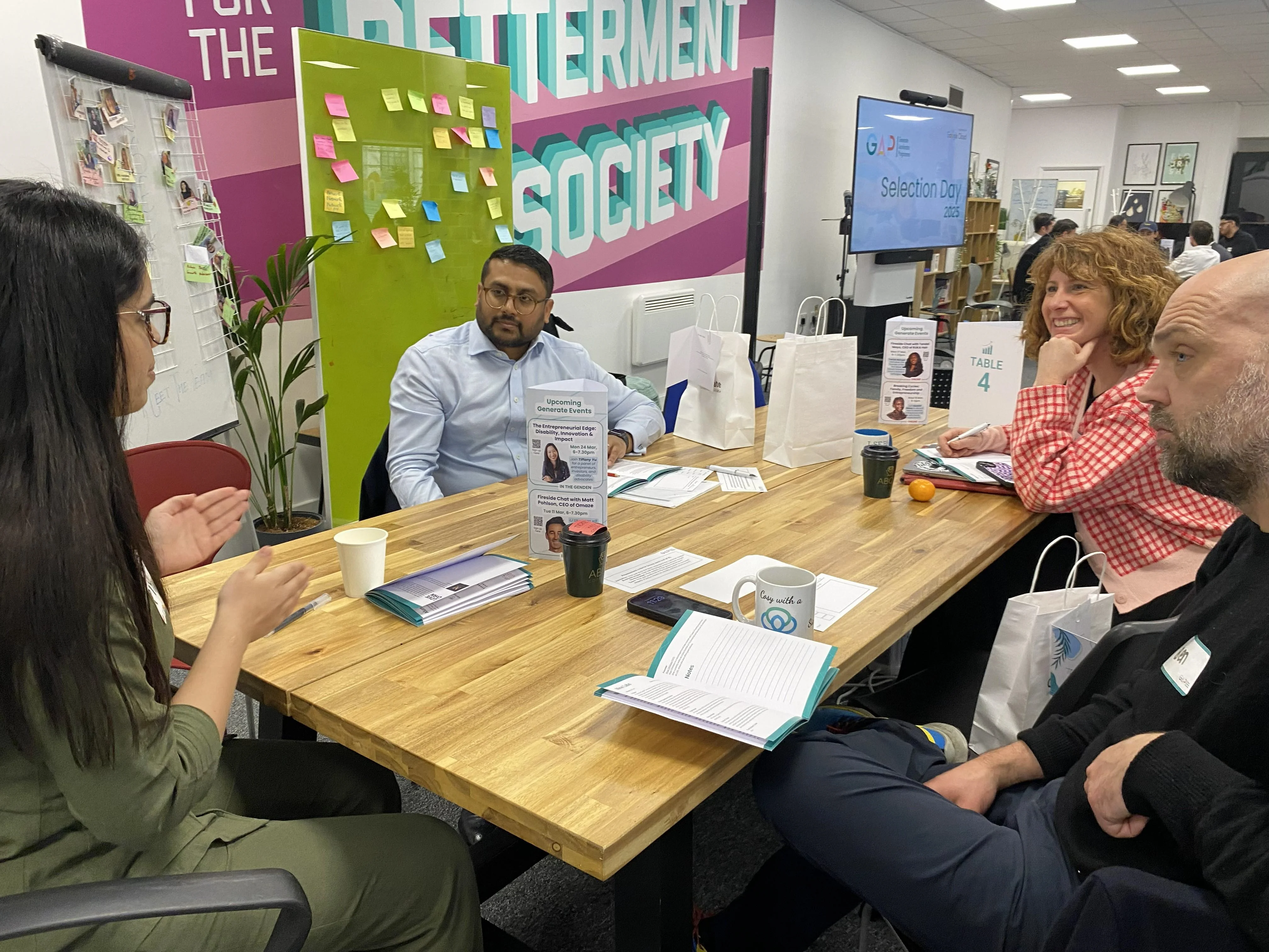 Four people sit around a table at the Gen Den discussing ideas,