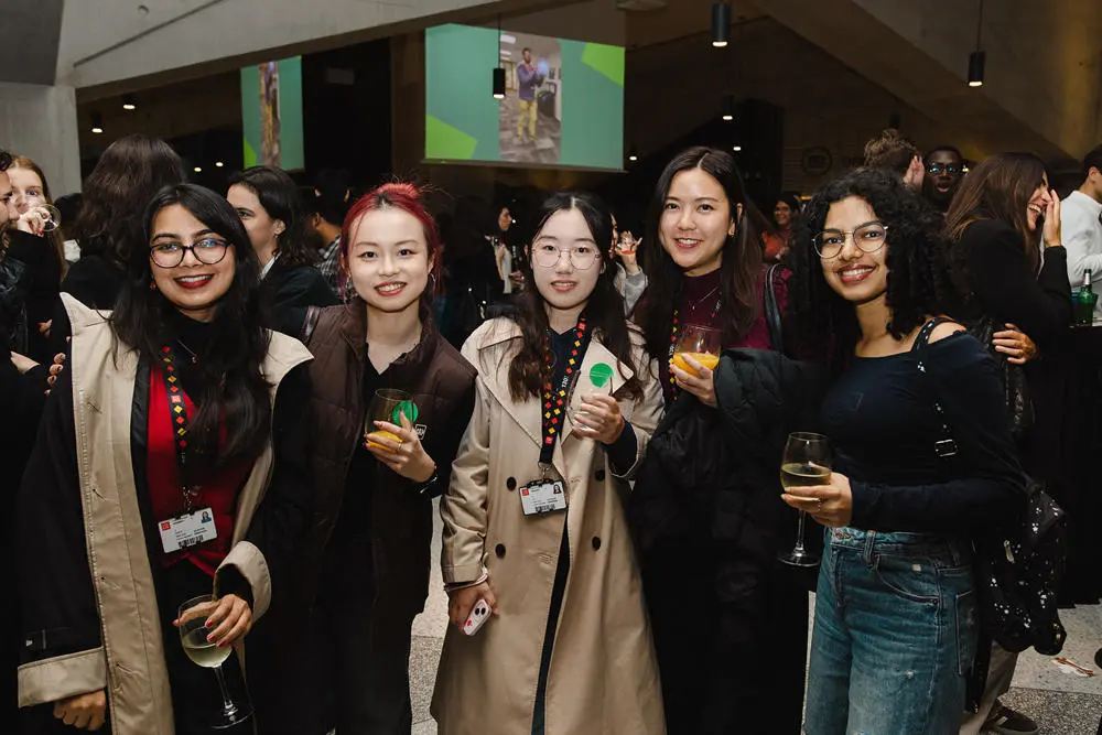 Five students at a Geography Welcome party holding drinks and smiling to camera