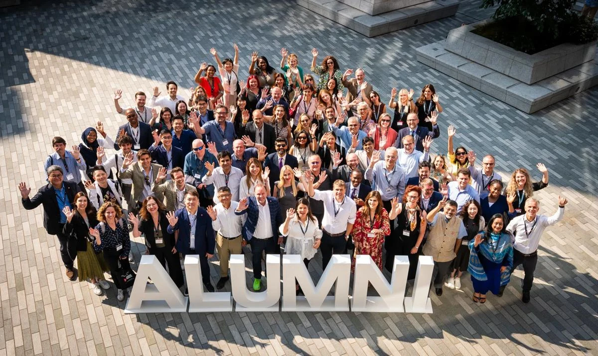 Many LSE alumni stand in the CBG square waving by some letters which spell "Alumni"