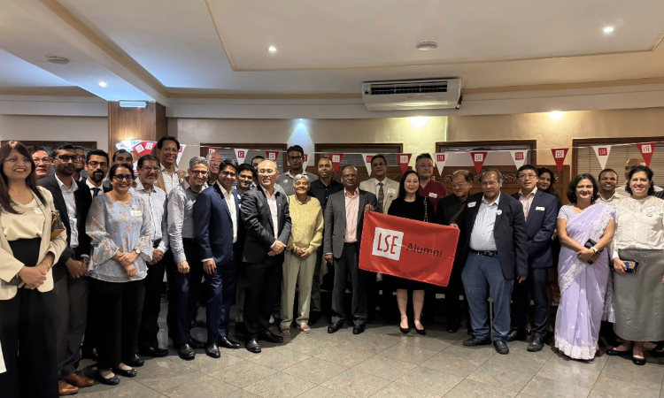 Large group of alumni gathered in front of LSE bunting and holding a LSE Alumni flag.