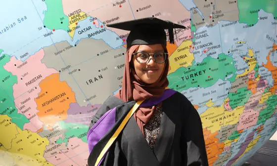 Graduating student wearing robes standing in front of LSE's globe