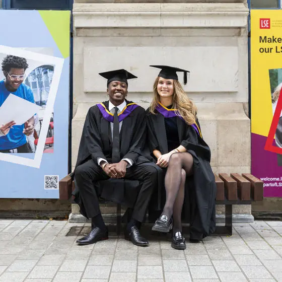 Two graduates sitting on a bench on LSE campus