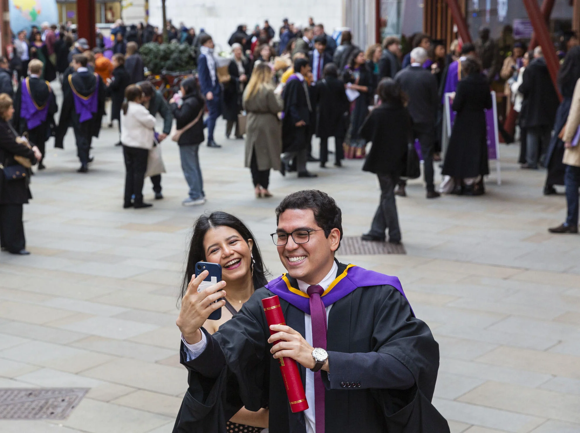 Male LSE graduate and female companion take a selfie in front of a crowd.