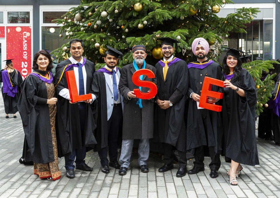 New graduates holding LSE letters in front of Christmas tree at December graduation