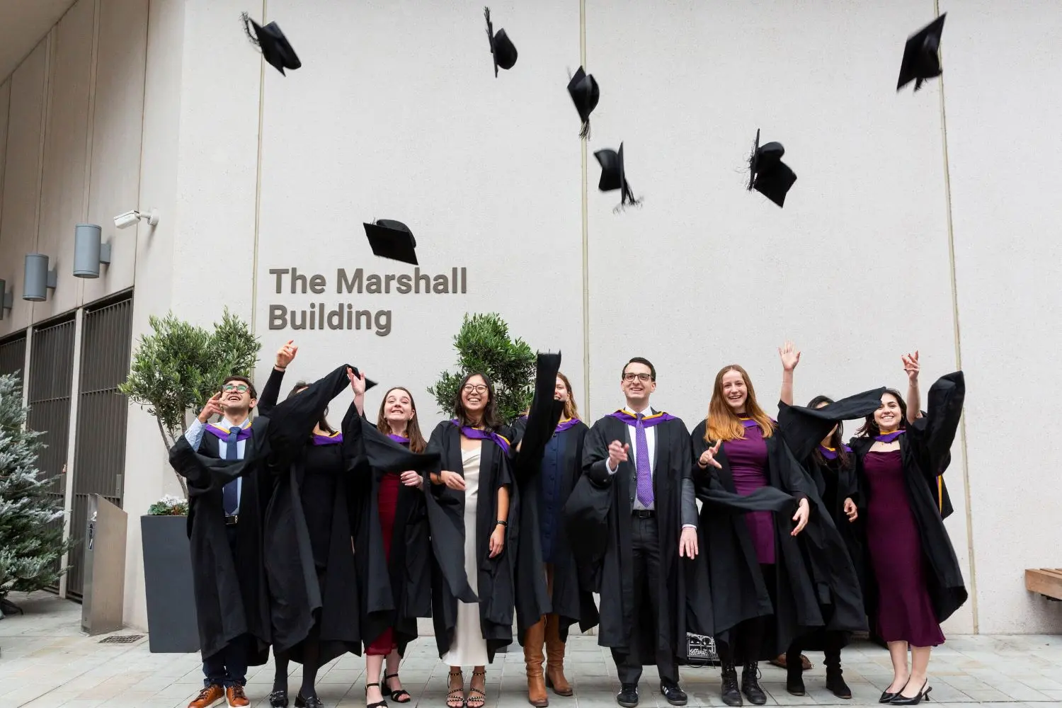 A group of students wearing graduation gowns throwing caps in the air.