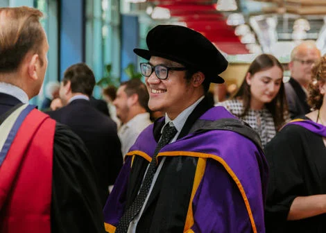 PhD graduate smiling in robes at a graduation reception in LSE's Centre Building.