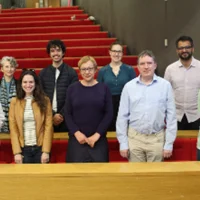 A group of nine people standing together in front of tiered red seating in a lecture theatre