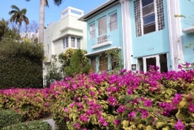 Bright pastel houses, balconies and large windows, set behind vivid pink flowering shrubs and greenery