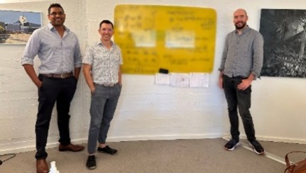 Three researchers  beside a presentation board with diagrams during a workshop or project discussion