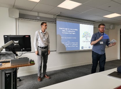 Two presenters beside a projected slide, addressing an audience during a workshop 