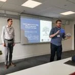 Two presenters beside a projected slide, addressing an audience during a workshop