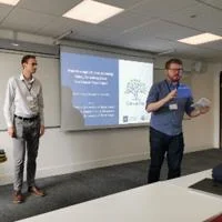 Two presenters beside a projected slide, addressing an audience during a workshop