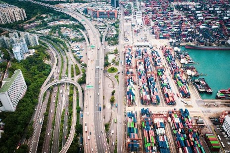 Aerial view of a busy container port filled with shipping containers beside multi-lane highway infrastructure 