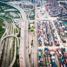 Aerial view of a busy container port filled with shipping containers beside multi-lane highway infrastructure