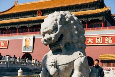 Stone guardian lion statue in front of a historic Chinese palace building with yellow roof and red walls