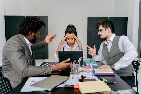 Tense office meeting with three colleagues in disagreement seated at a desk in an office environment