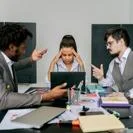 Tense office meeting with three colleagues in disagreement seated at a desk in an office environment