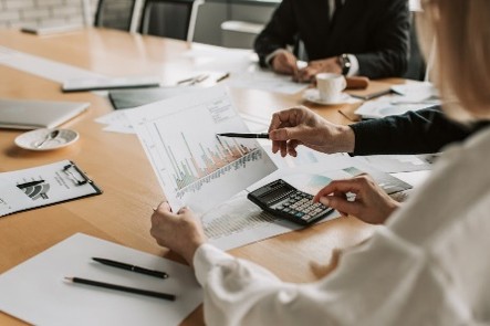 Professionals seated at a conference table reviewing printed financial charts using a calculator during a meeting.