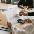 Professionals seated at a conference table reviewing printed financial charts using a calculator during a meeting.