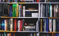 Bookshelf filled with tightly packed books of various sizes and colours, arranged upright and stacked horizontally