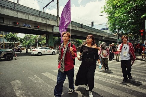 Street protest with pedestrians crossing an urban intersection while carrying a purple banner