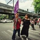 Street protest with pedestrians crossing an urban intersection while carrying a purple banner
