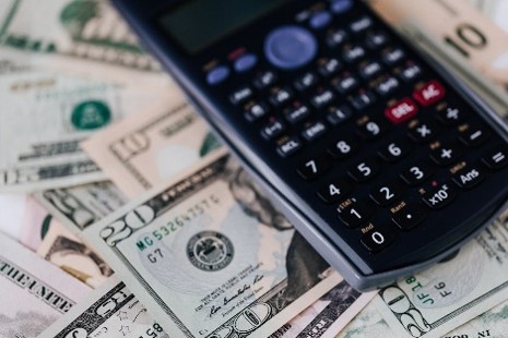 Calculator on a spread of US dollar banknotes of two denominations representing finance, budgeting, and cost analysis