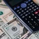 Calculator on a spread of US dollar banknotes of two denominations representing finance, budgeting, and cost analysis
