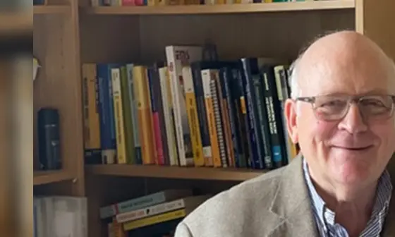 Henry Wynn sitting at a desk, pen in hand, with a bookshelf behind him.