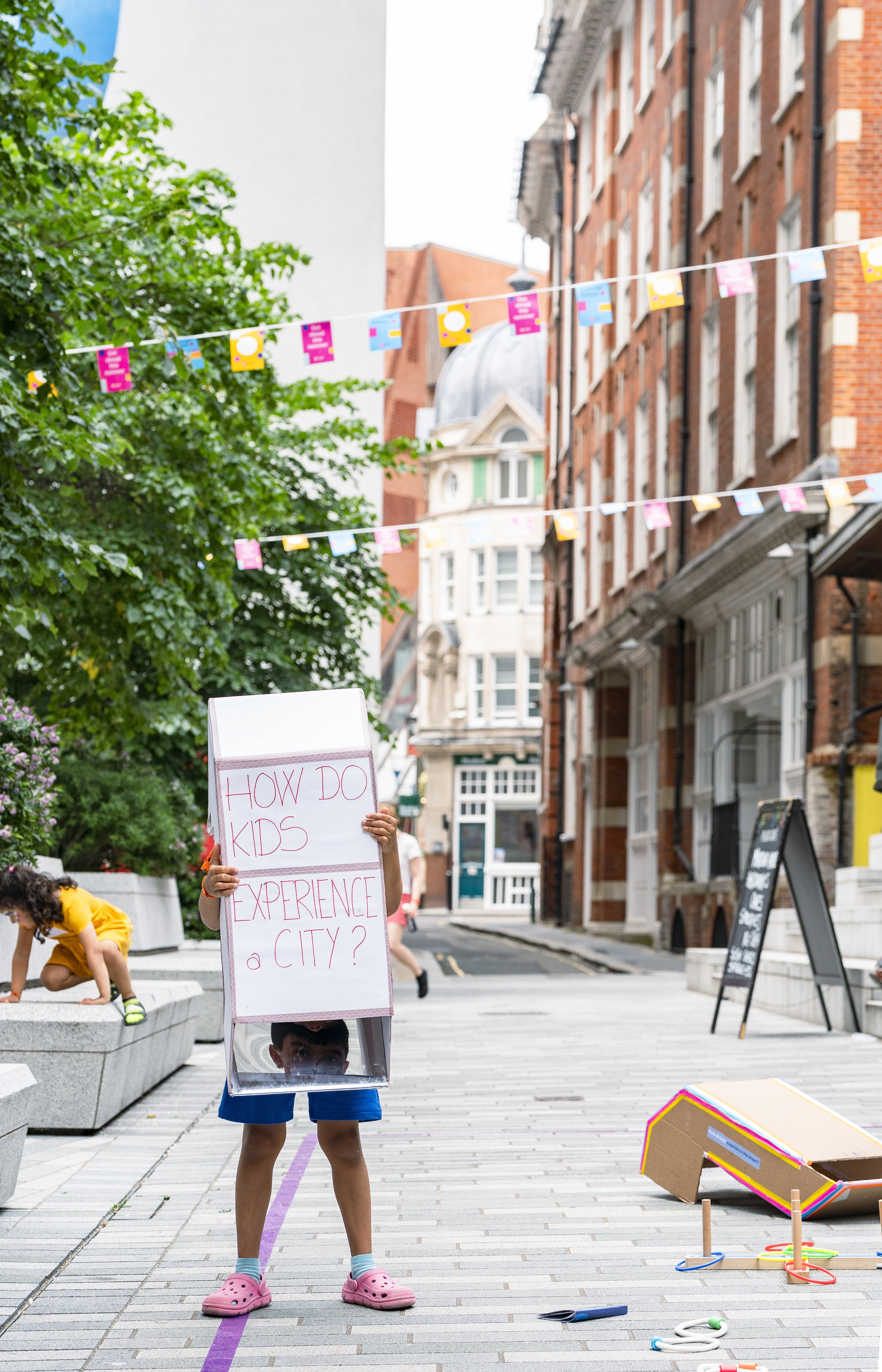 A child holding up a sign saying "How do kids experience a city"