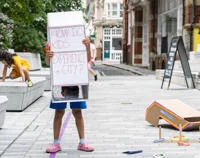 A child holding up a sign saying "How do kids experience a city"