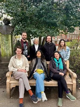 a group of seven people sit and smile at the camera