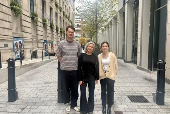 three people stand in the middle of a street, smiling at the camera