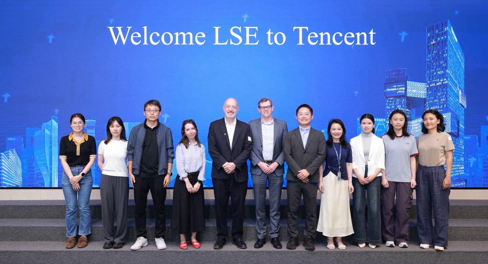 A group of individuals pose in a line for a photo in front of a screen that says 'Welcome LSE to Tencent.' 
