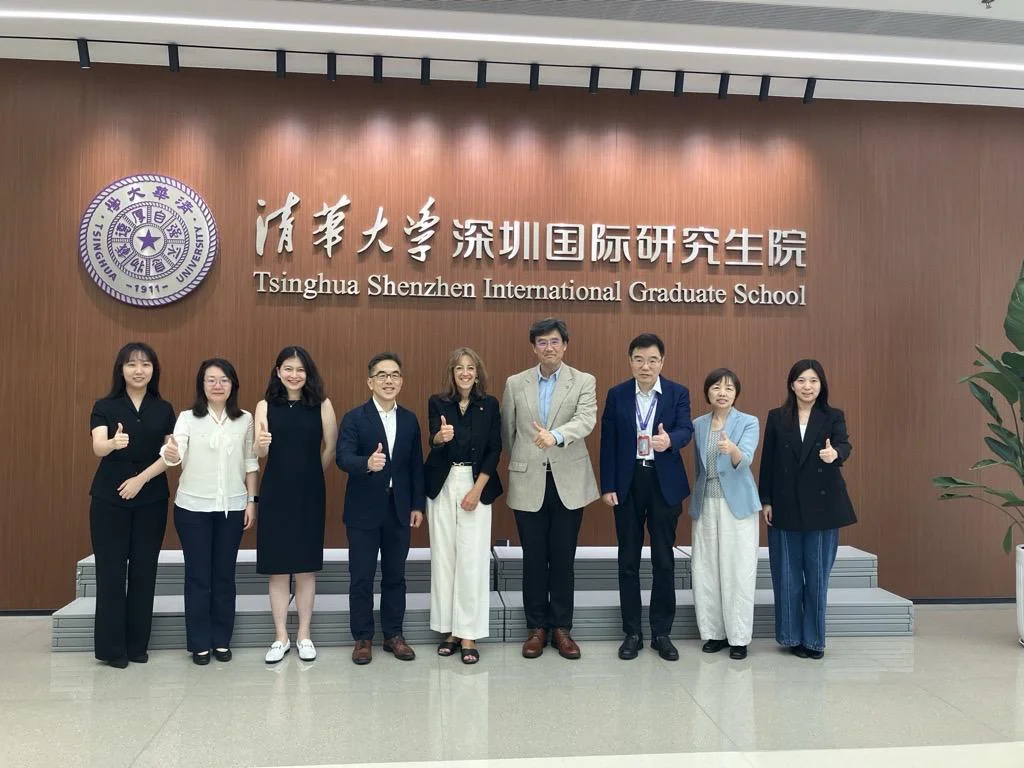 A group of nine individuals posed in front of a wall with the Tsinghua Shenzhen International Graduate School logo.