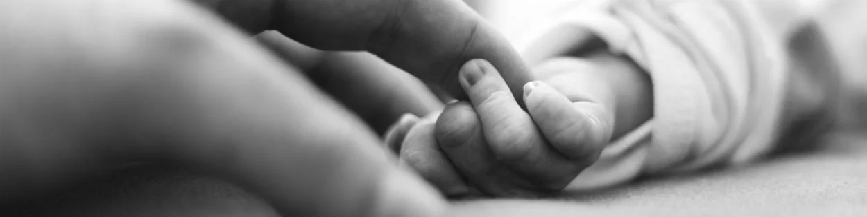 A black and white image of an adult hand holding a baby hand