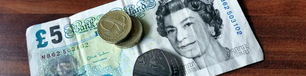 A UK sterling £5 note with some coins