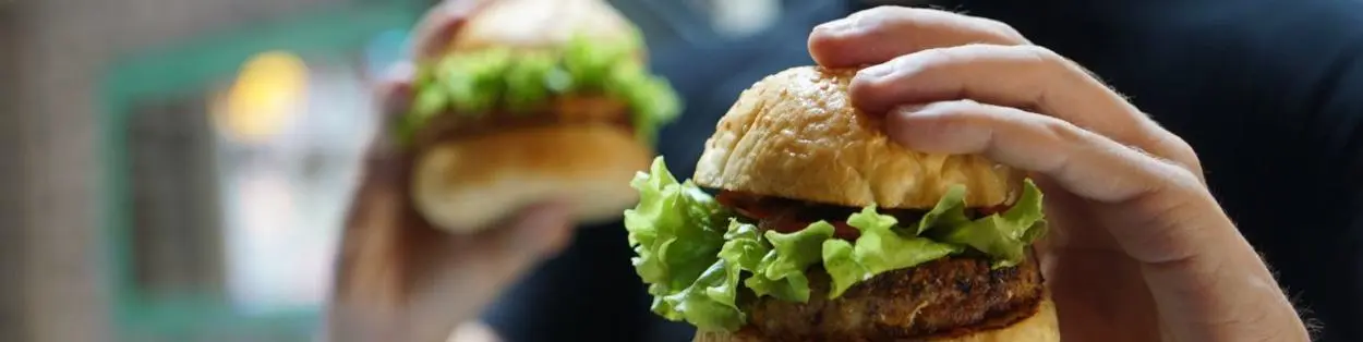 A person holding a burger in each hand.