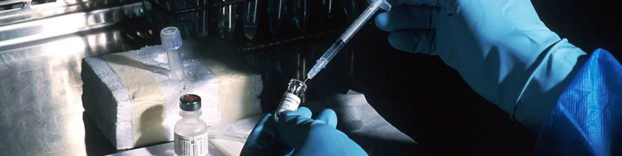 A scientists using an injection to remove medicine from a tube.
