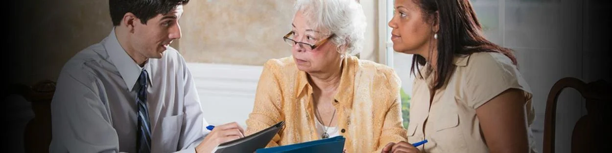 A man in a suit talking with an elderly woman and another younger woman going through paperwork.