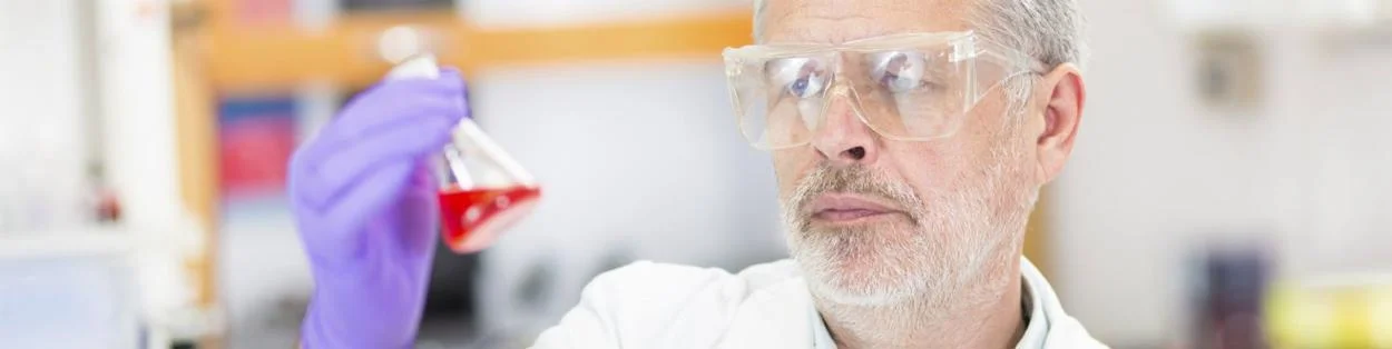 a man wearing science goggles and holding a glass of liquid