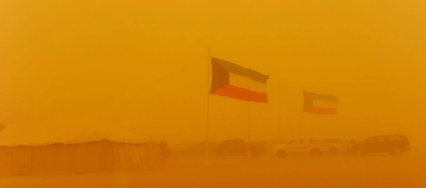 A hot and dusty scene with Kuwaiti flags hazy in the orange sand.