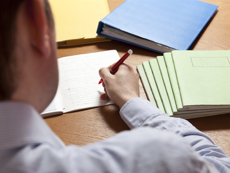 Over the shoulder photo of man marking yellow exam booklets