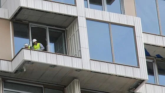 Two workmen in health and safety gear on the balcony of a newbuild flat