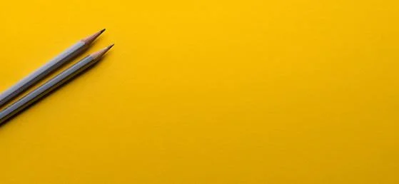 Two grey pencils against a yellow background