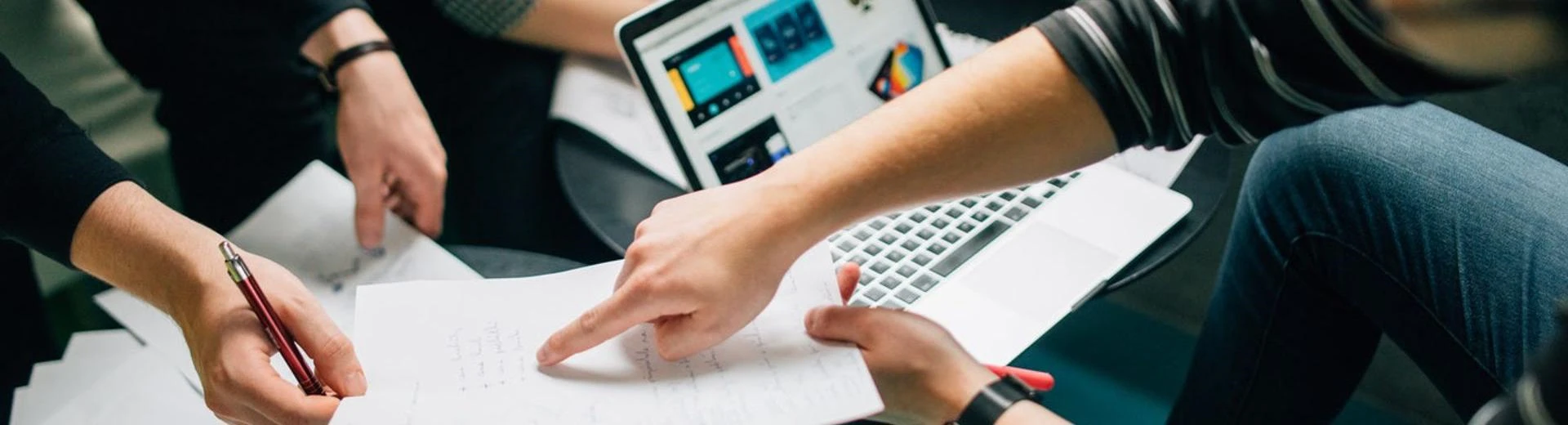 group of students sit around a laptop and point at pieces of paper