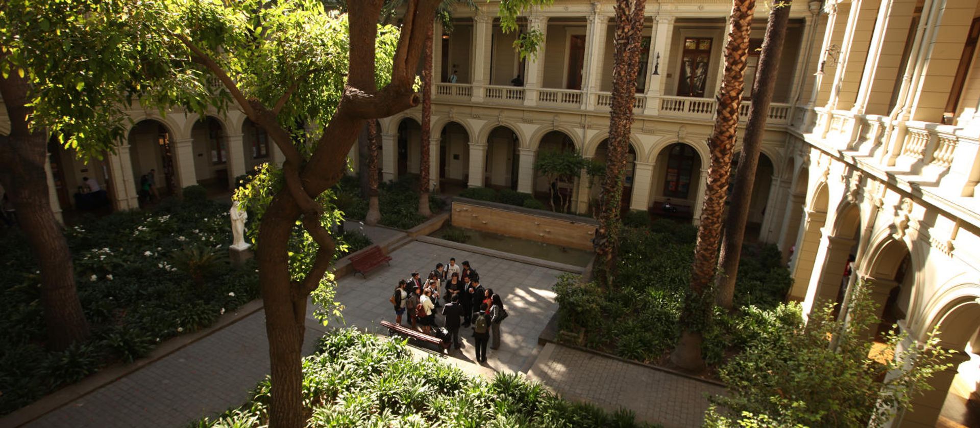 UC Chile University courtyard with trees and a huddle of students in sunlight