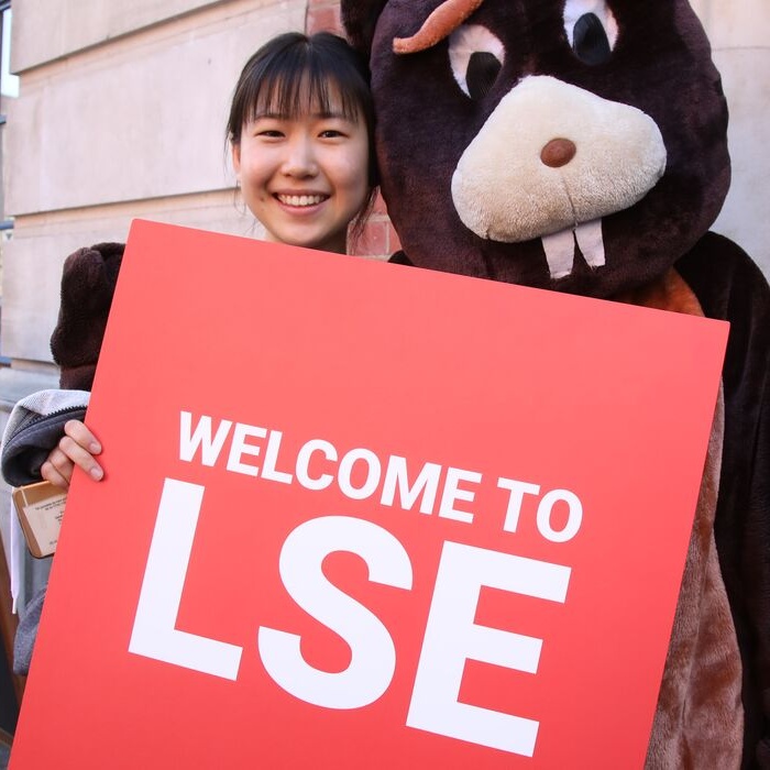 Smiling student and beaver mascot hold Welcome to LSE sign