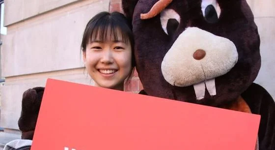 Smiling student and beaver mascot hold Welcome to LSE sign